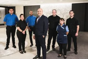 A team of seven professionals in uniforms stands confidently in a modern office, ready for cleaning duties.