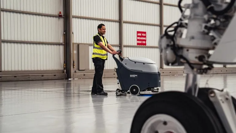 Cleaner in high-vis using a scrubber dryer in an airport hanger
